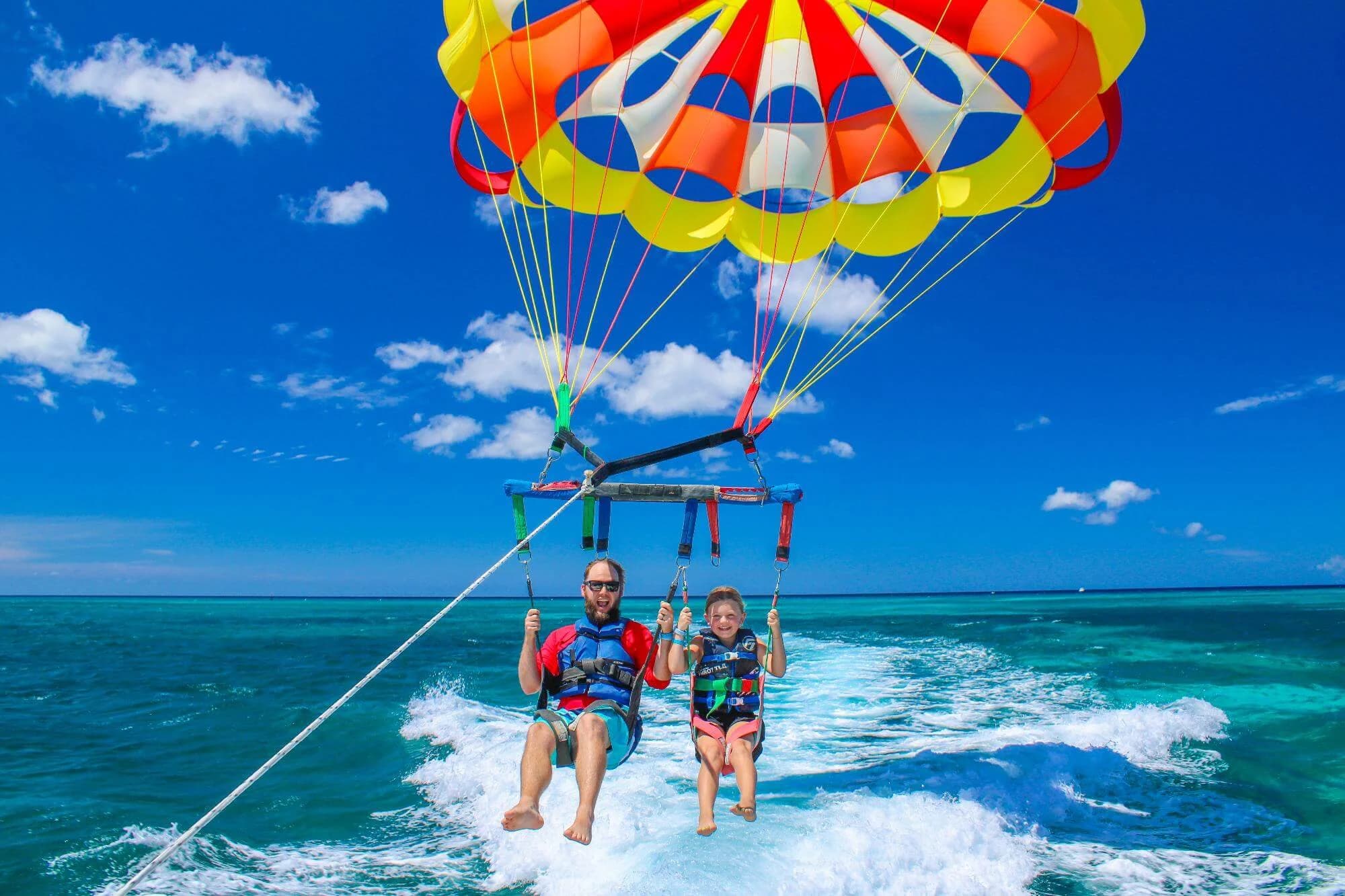 Two guests beneath the crew’s multicolored parasail over the sea off Palm Beach, Aruba